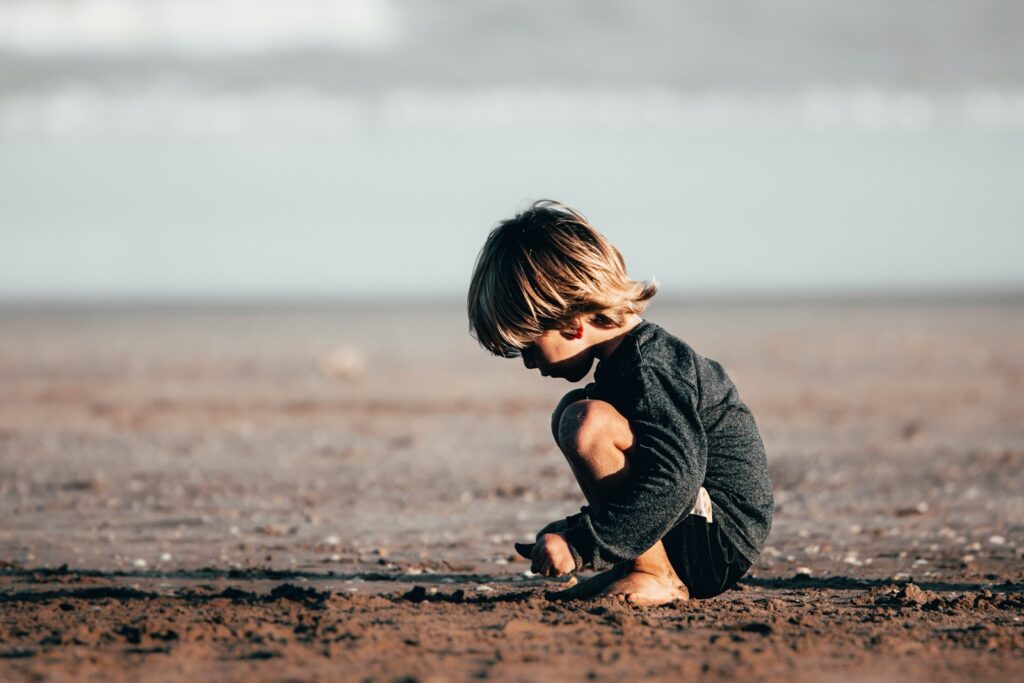 girl in gray hoodie sitting on brown sand during daytime